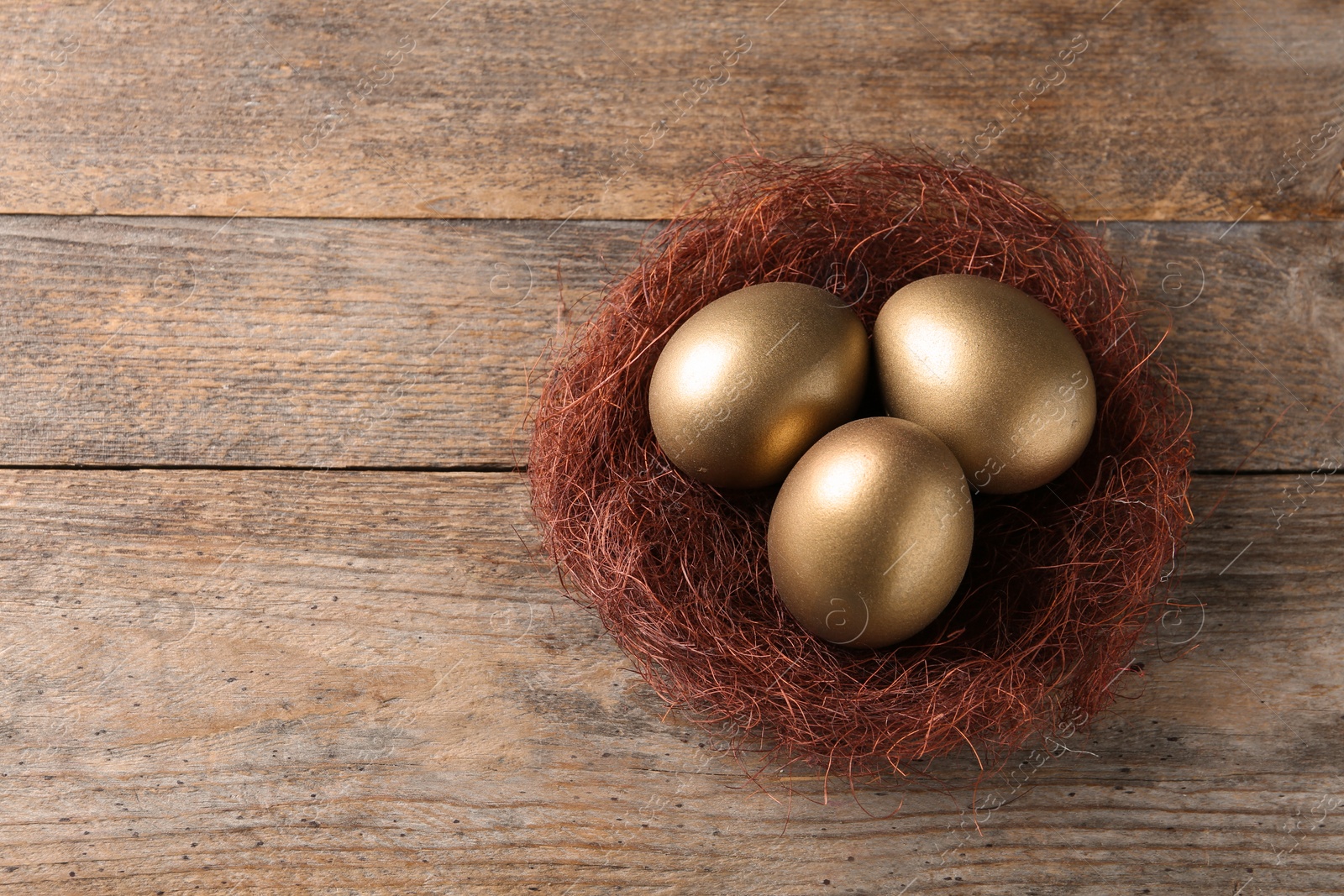 Photo of Golden eggs in nest on wooden background, top view with space for text