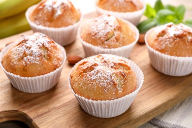 Photo of Tasty muffins powdered with sugar on wooden board, closeup