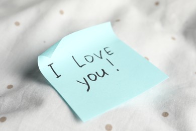 Photo of Sticky note with phrase I love you! on bed, closeup