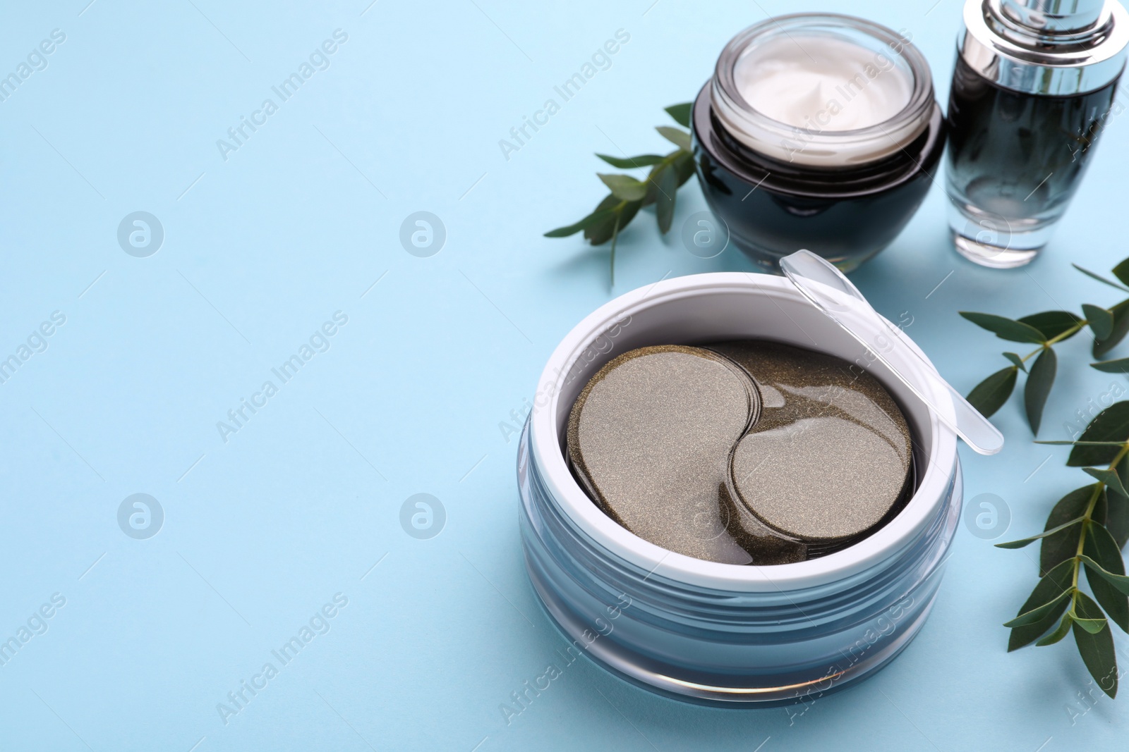 Photo of Under eye patches and other cosmetic products on light blue background. Space for text