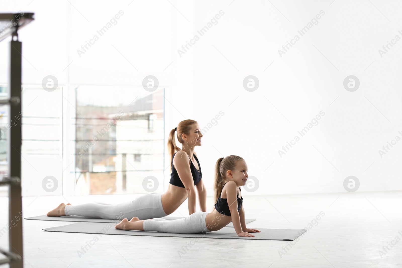 Photo of Mother and daughter in matching sportswear doing yoga together at home