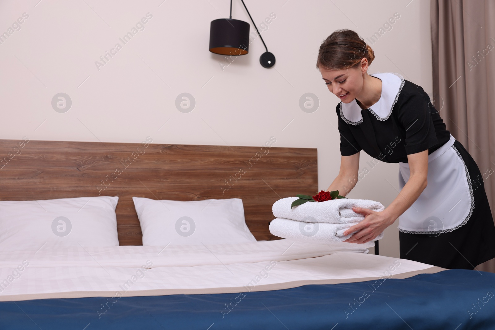 Photo of Beautiful chambermaid putting fresh towels on bed in hotel room