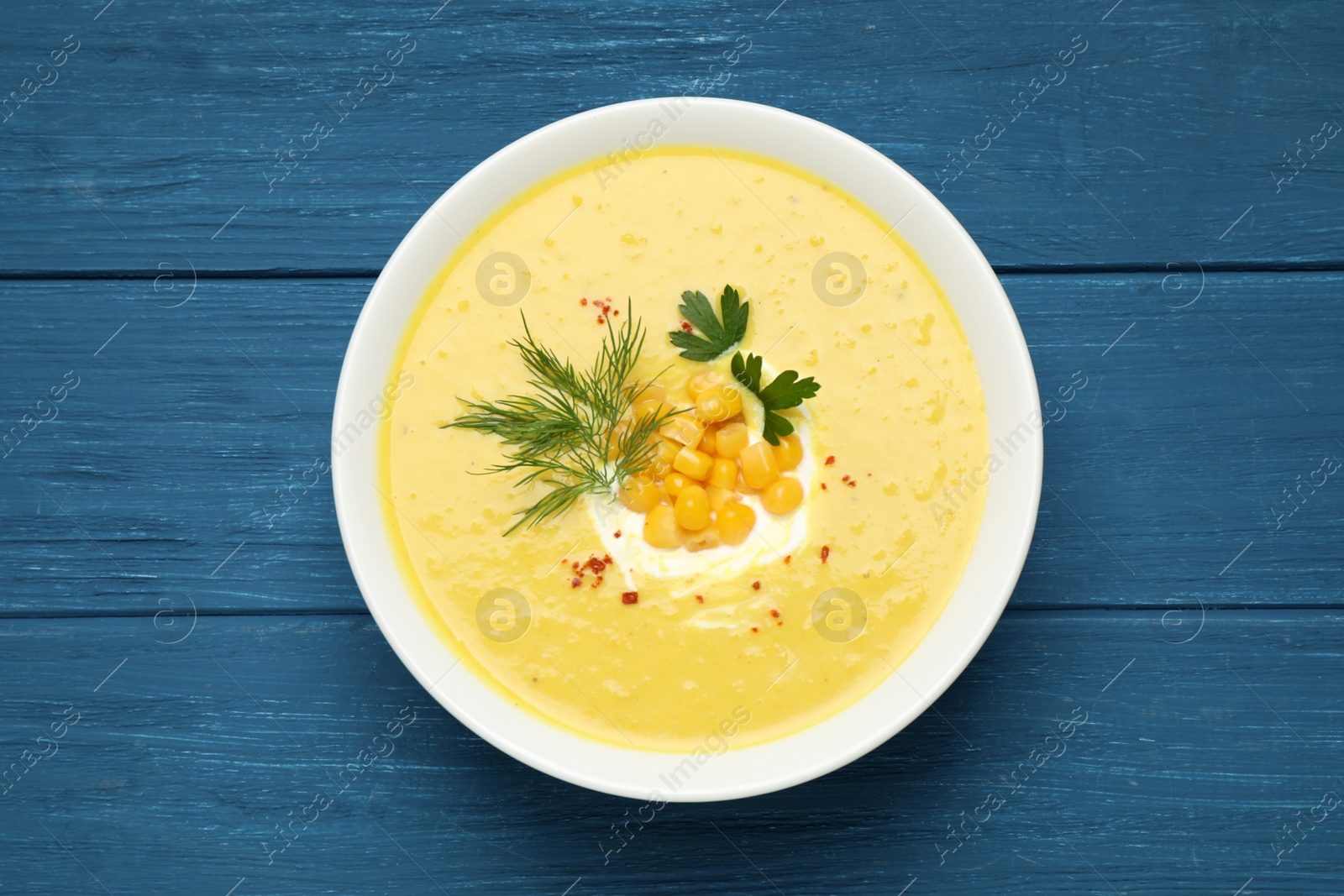 Photo of Delicious creamy corn soup served on blue wooden table, top view