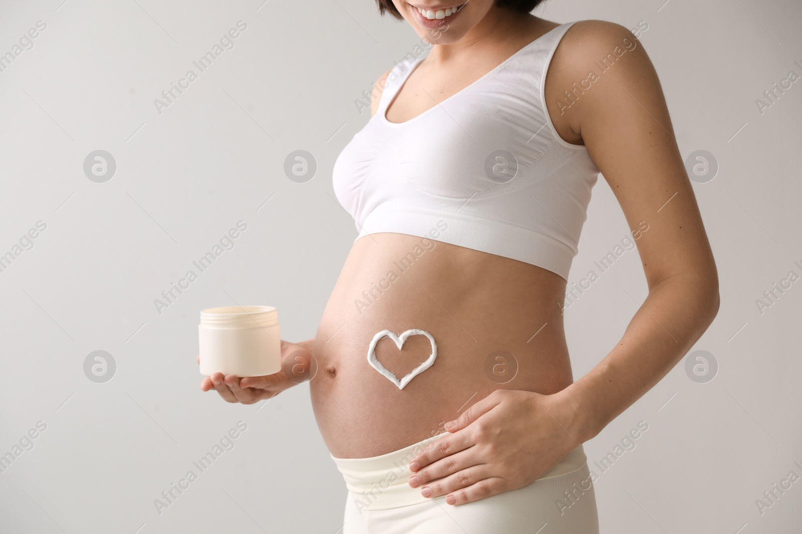Photo of Young pregnant woman with cosmetic product on grey background, closeup