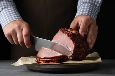 Photo of Man cutting ham on wooden board at table, closeup
