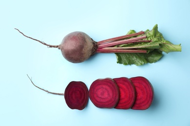 Whole and cut fresh red beets on light blue background, flat lay