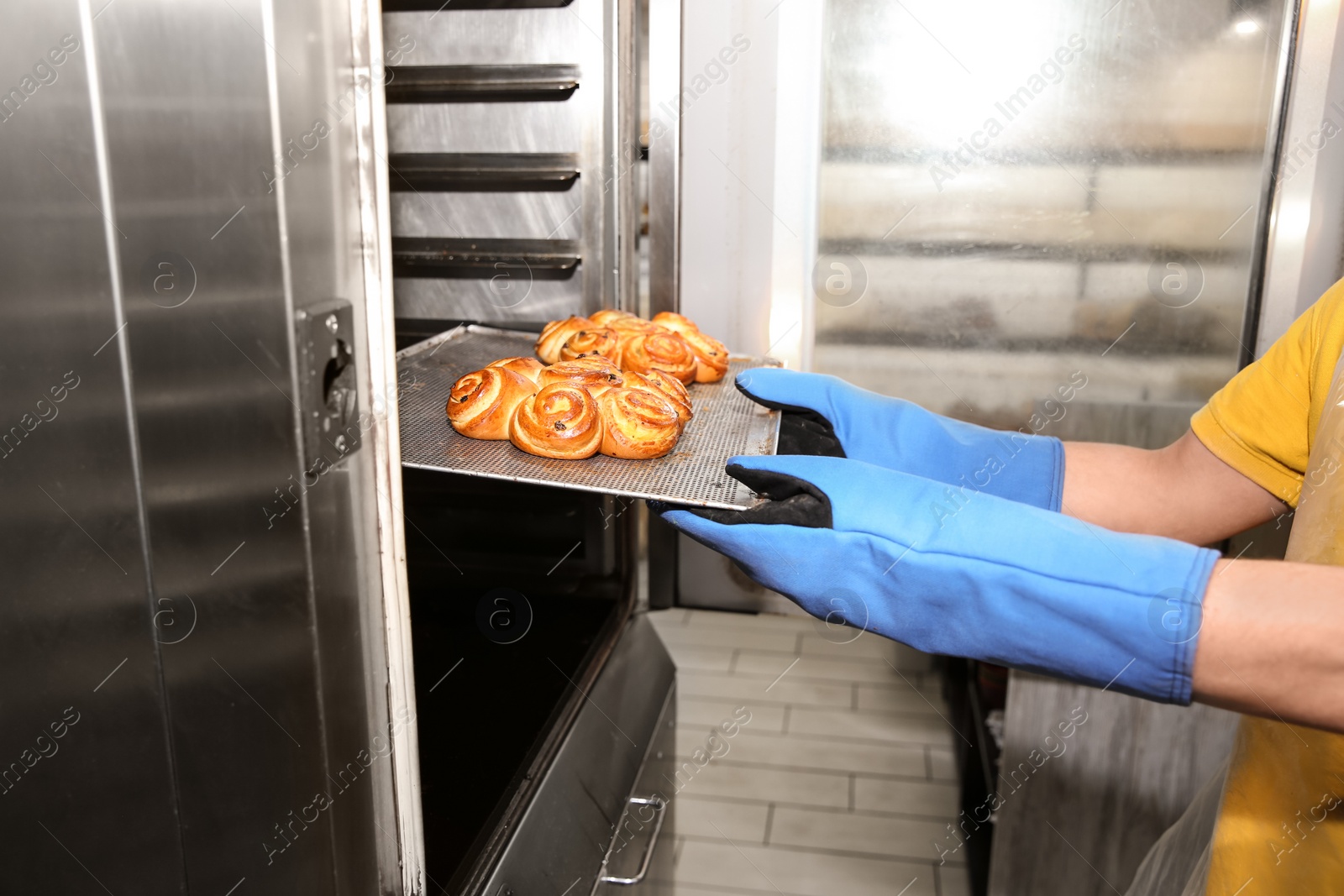 Photo of Baker taking out tray with pastry from oven in workshop, closeup