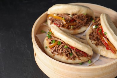 Delicious gua bao in bamboo steamer on black table, closeup. Space for text