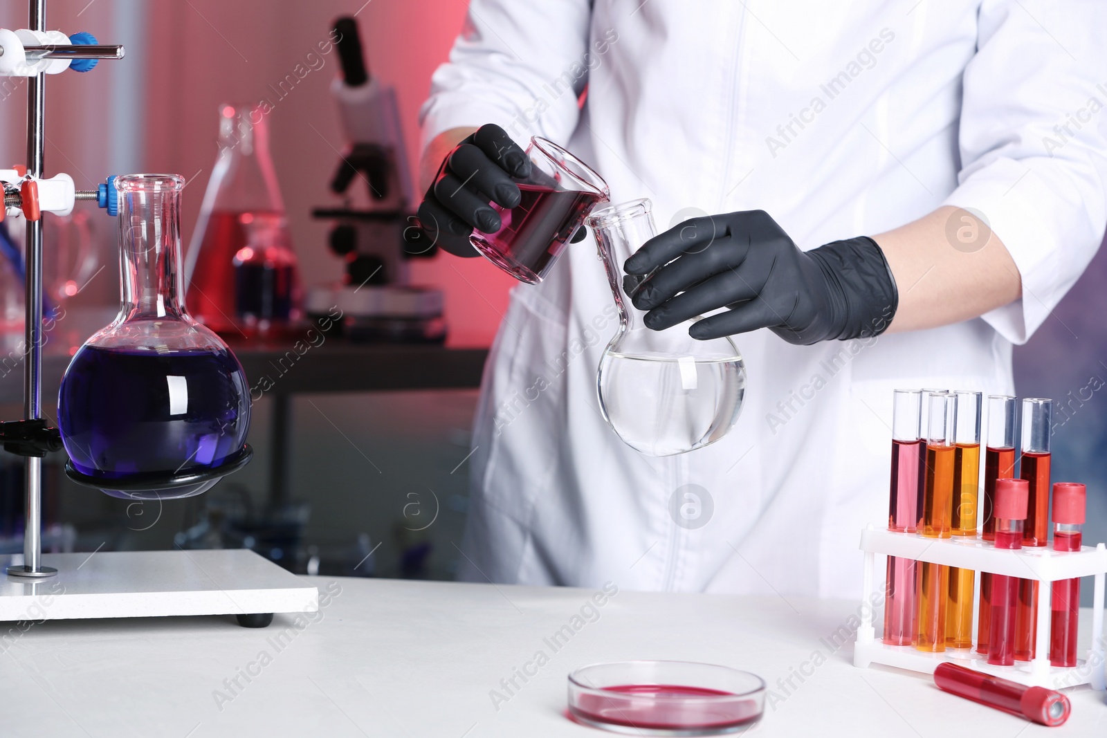 Photo of Scientist pouring reagent into flask at table in chemistry laboratory