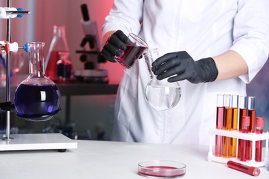 Scientist pouring reagent into flask at table in chemistry laboratory