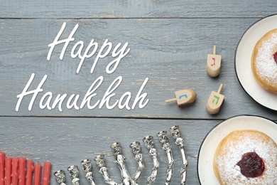 Image of Happy Hanukkah. Flat lay composition with menorah, red candles, dreidels and sufganiyot on grey wooden table