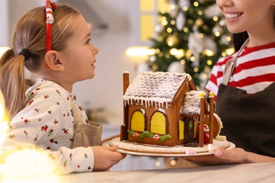 Photo of Mother and daughter with gingerbread house in kitchen, closeup
