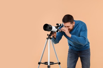 Photo of Astronomer looking at stars through telescope on beige background. Space for text
