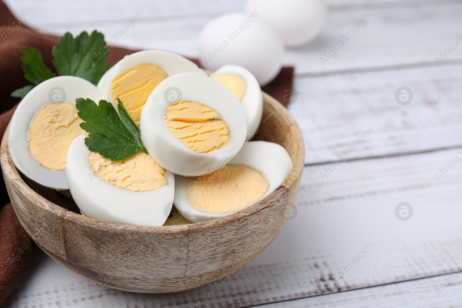 Photo of Fresh hard boiled eggs and parsley on white wooden table, closeup. Space for text