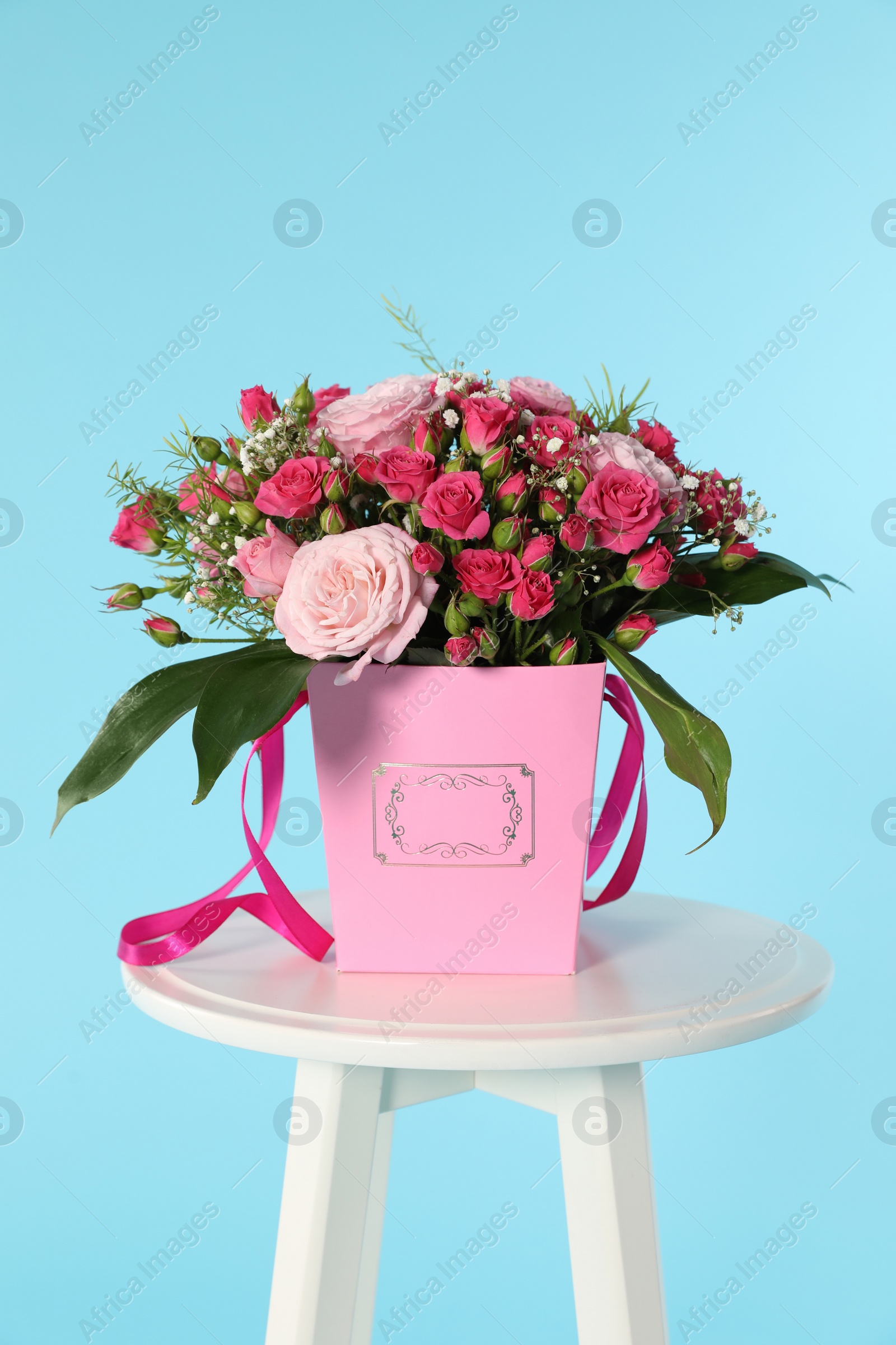 Photo of Beautiful bouquet of flowers in paper gift box on table against color background