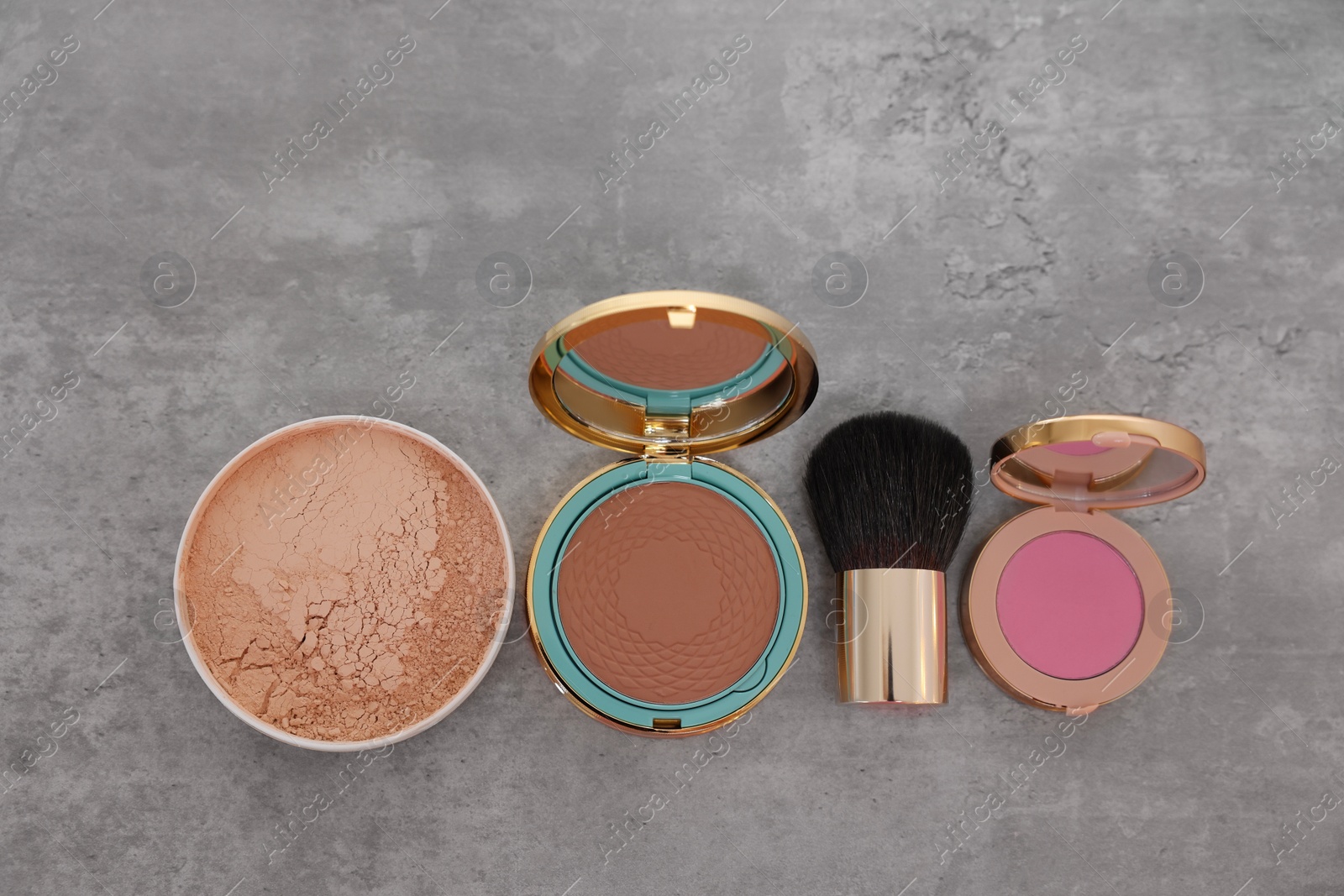 Photo of Bronzer, powder, blusher and brush on grey textured table, flat lay