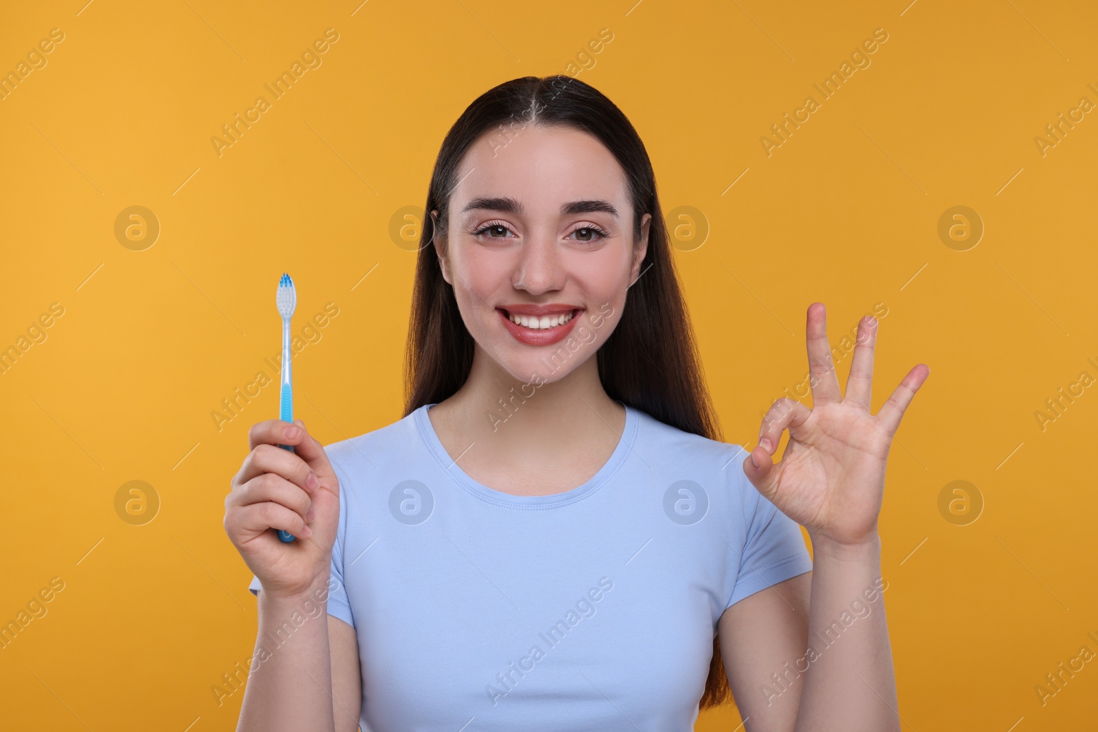 Photo of Happy young woman holding plastic toothbrush and showing OK gesture on yellow background