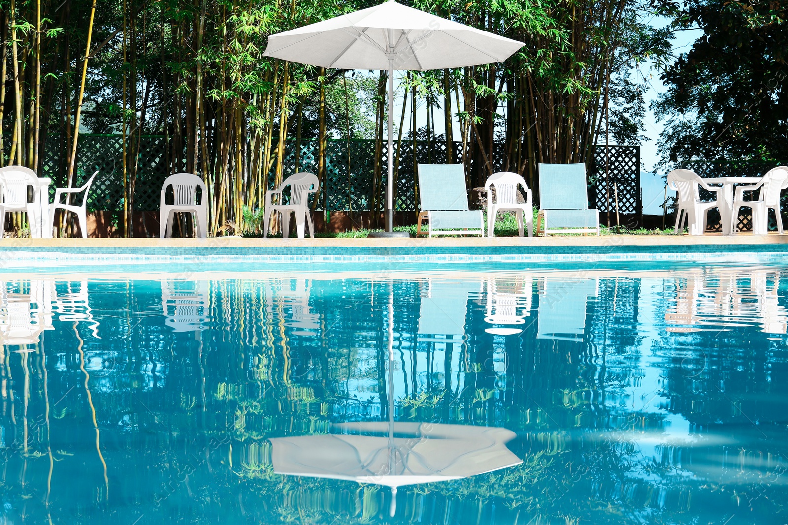 Photo of Pool with clean water, sunbeds and parasol outdoors