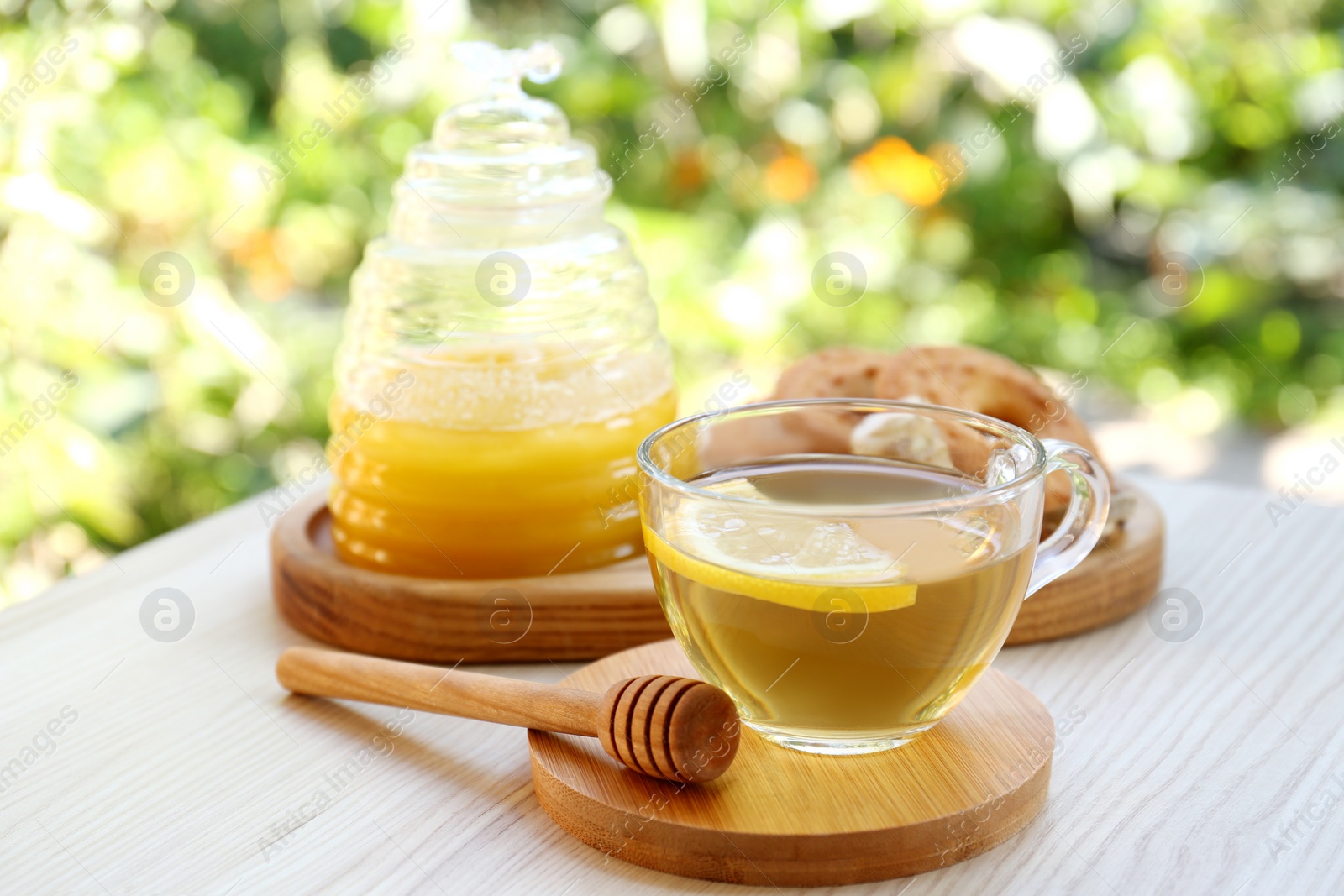 Photo of Cup of delicious tea with lemon and honey on wooden table outdoors