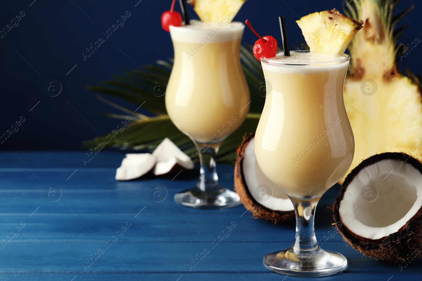 Photo of Tasty Pina Colada cocktails and ingredients on blue wooden table, space for text