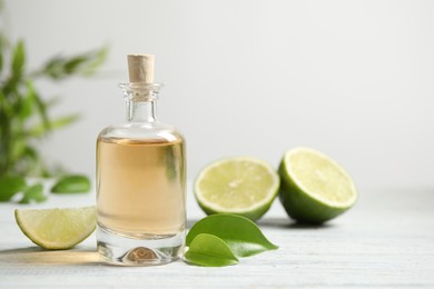 Photo of Lime essential oil and cut fruits on white wooden table. Space for text