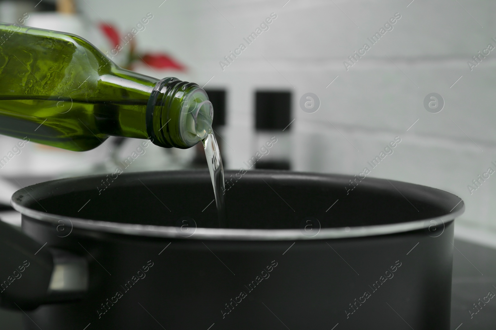 Photo of Pouring cooking oil from bottle into saucepan in kitchen, closeup