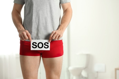 Photo of Man holding SOS sign indoors, space for text. Urology problems