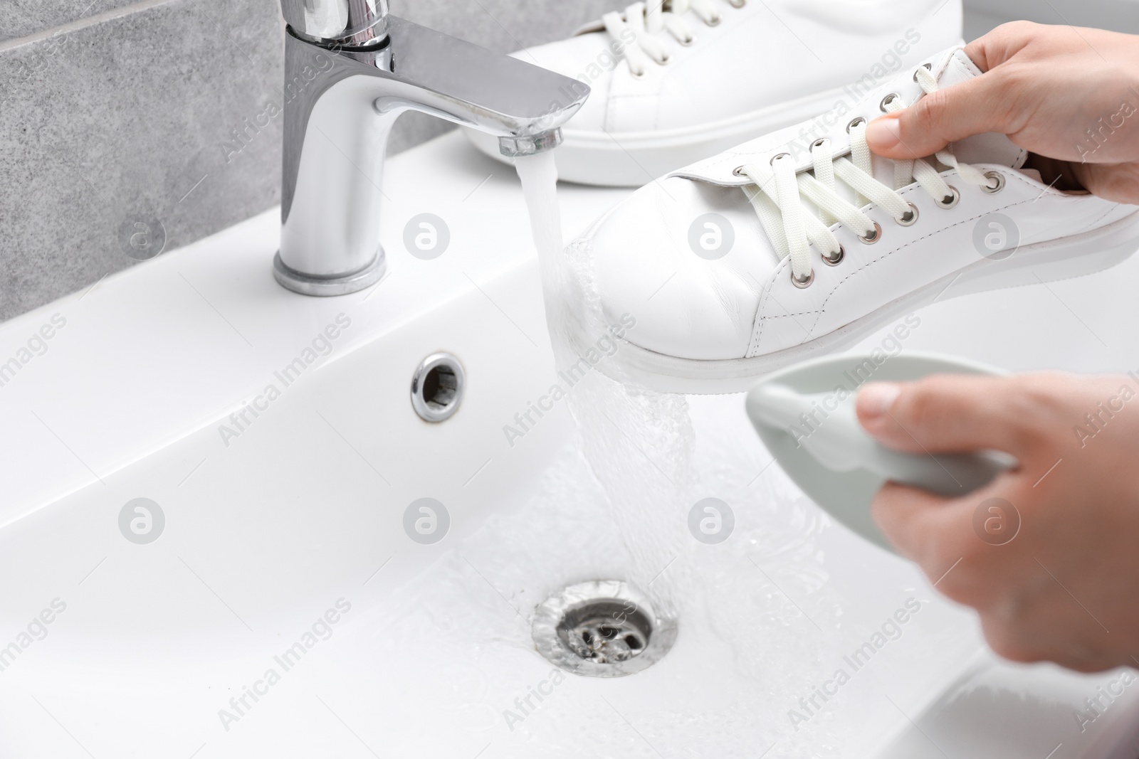 Photo of Woman washing stylish sneakers with brush in sink, closeup