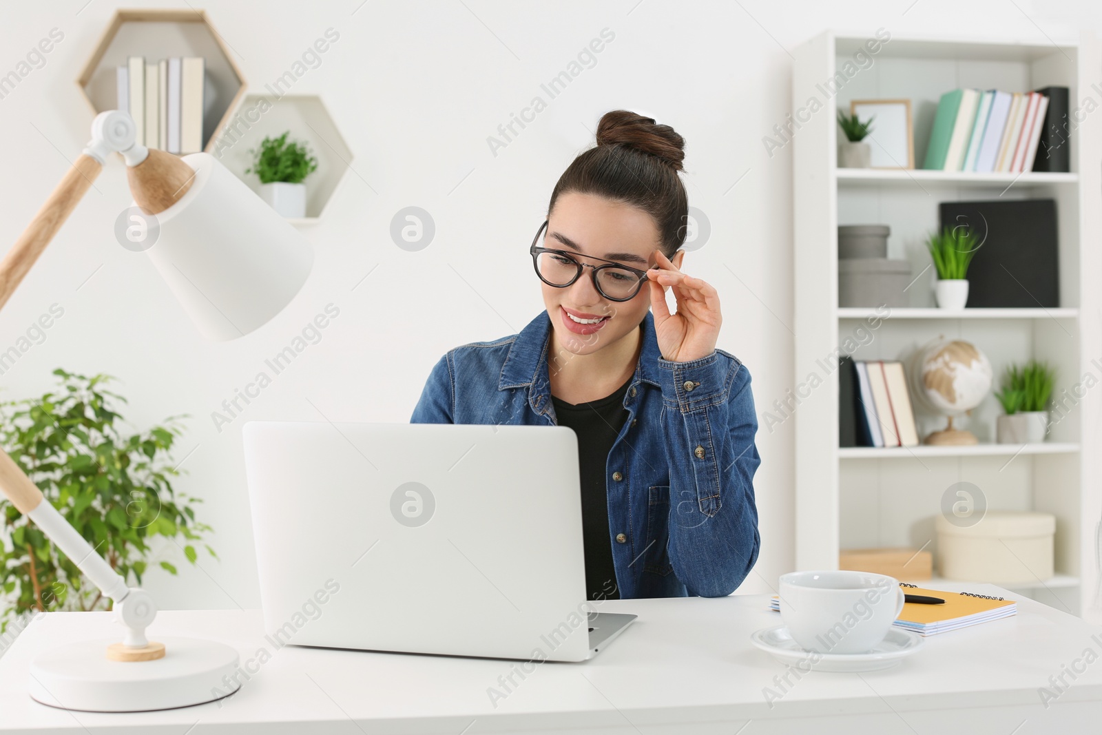 Photo of Home workplace. Happy woman working on laptop at white desk in room