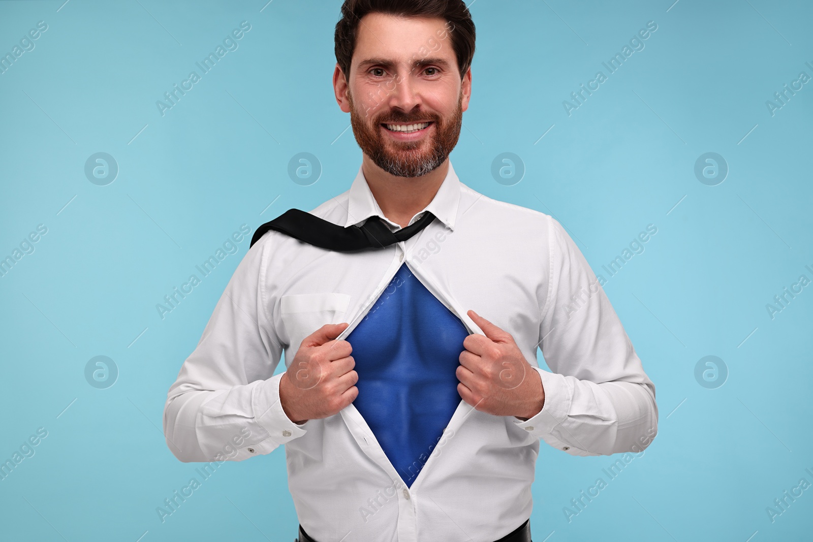 Image of Happy businessman wearing superhero costume under suit on light blue background