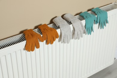 Photo of Modern radiator with knitted gloves near beige wall indoors