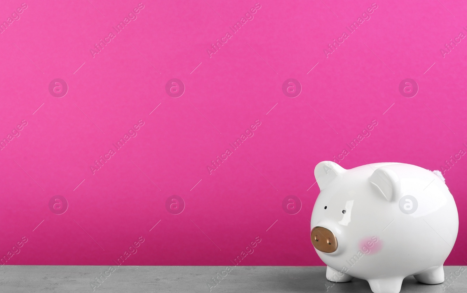 Photo of White piggy bank on light grey table against pink background. Space for text