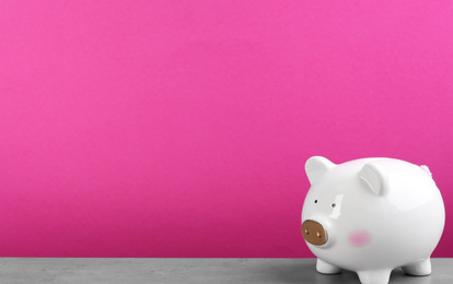 White piggy bank on light grey table against pink background. Space for text