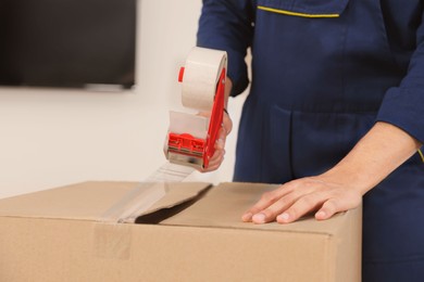 Photo of Male mover packing box with adhesive tape indoors, closeup