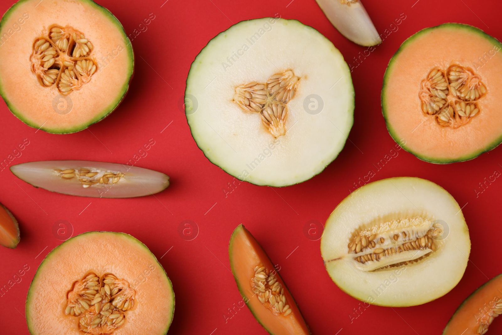 Photo of Cut different types of melons on red background, flat lay