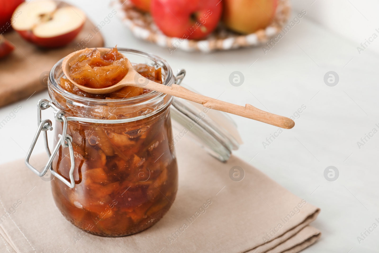 Photo of Delicious apple jam in jar and wooden spoon on table