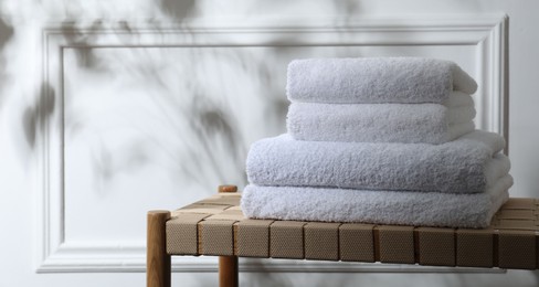 Photo of Stacked terry towels on wicker bench indoors, space for text