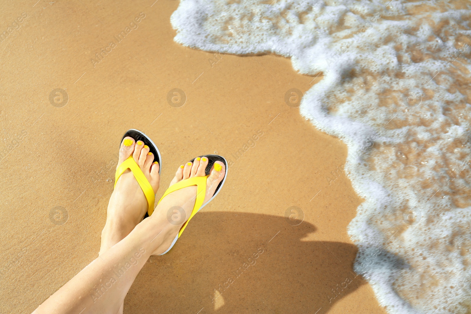 Photo of Closeup of woman with flip flops on sand near sea, space for text. Beach accessories