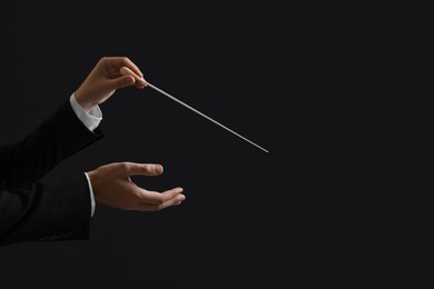 Professional conductor with baton on black background, closeup. Space for text