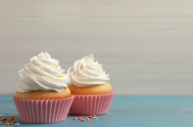 Photo of Delicious cupcakes decorated with cream on light blue wooden table, space for text