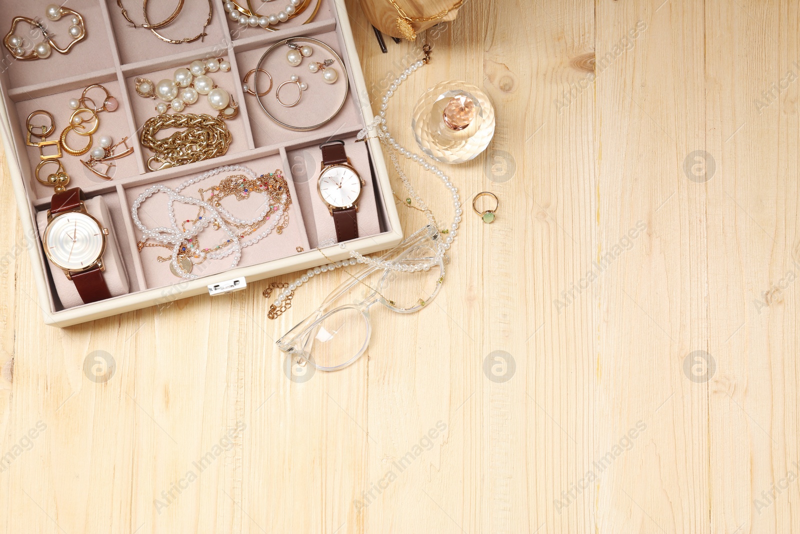 Photo of Jewelry box with many different accessories, perfume and glasses on light wooden table, flat lay. Space for text