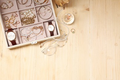 Jewelry box with many different accessories, perfume and glasses on light wooden table, flat lay. Space for text