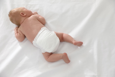 Cute little baby in diaper on bed, top view