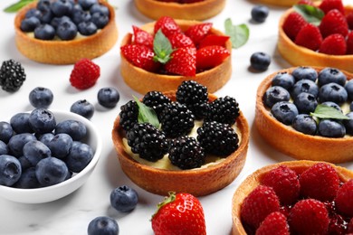 Photo of Tartlets with different fresh berries on white marble table. Delicious dessert