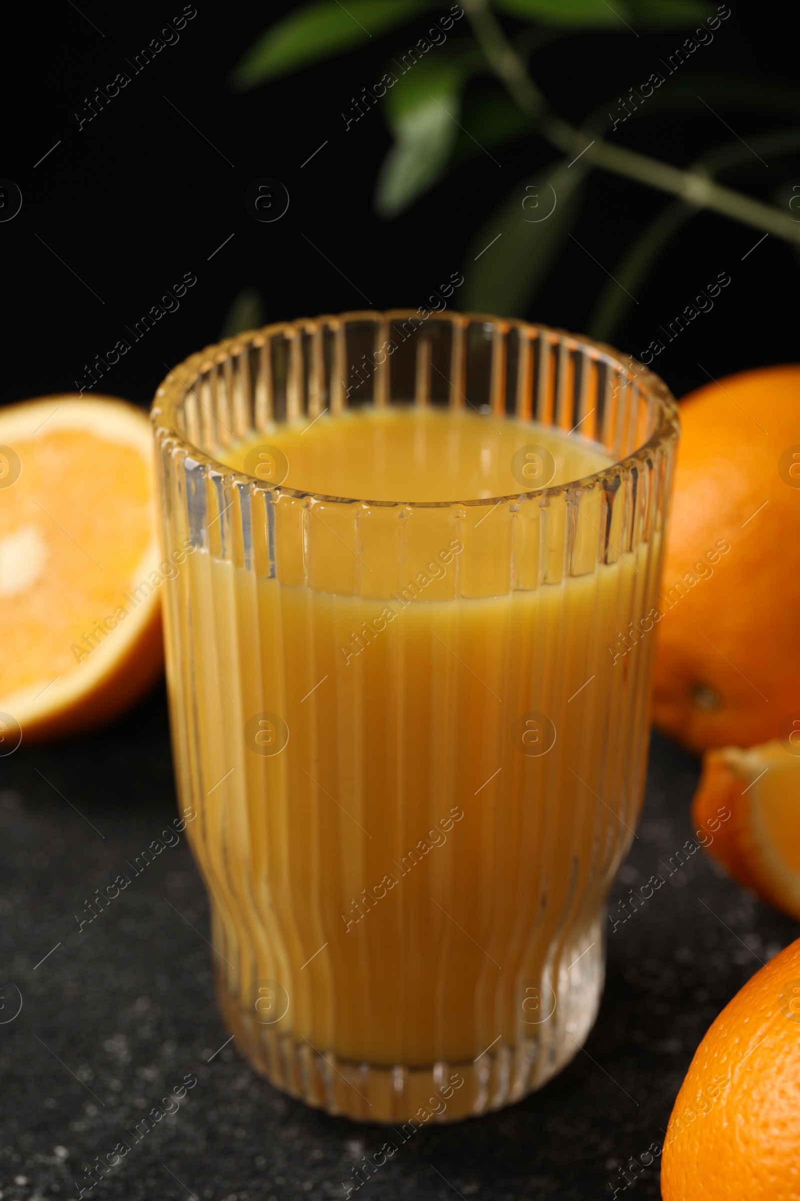 Photo of Tasty fresh oranges, juice and leaves on black table, closeup