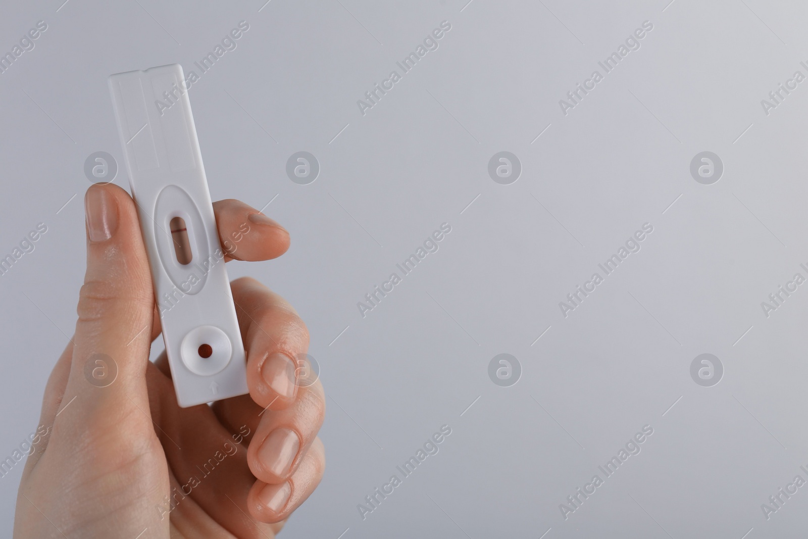 Photo of Woman holding disposable express test on light grey background, closeup. Space for text