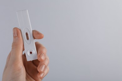 Photo of Woman holding disposable express test on light grey background, closeup. Space for text