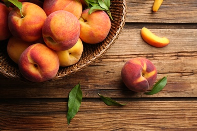 Photo of Fresh sweet peaches in wicker basket on wooden table, flat lay
