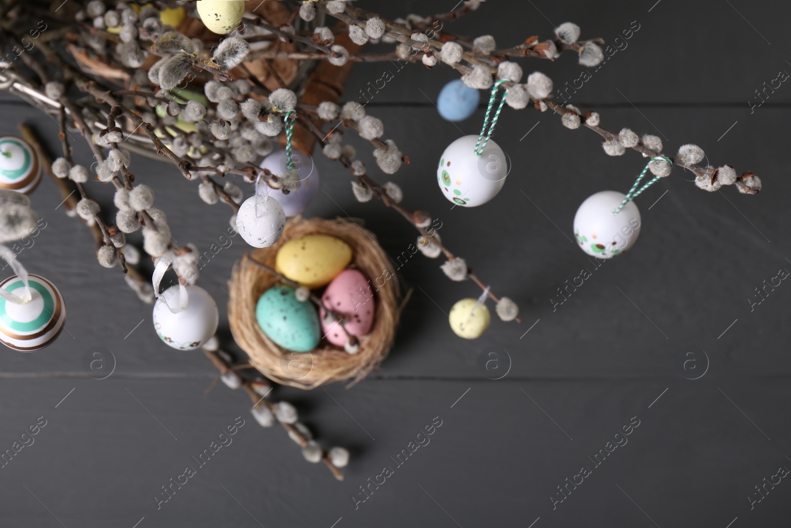 Photo of Beautiful willow branches with painted eggs and Easter decor on light grey wooden table, above view