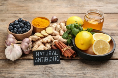 Photo of Different fresh products and card with phrase Natural Antibiotic on wooden table